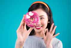 亚洲美女孩持有粉红色的甜甜圈眼睛复古的快乐的女人糖果甜点站蓝色的背景