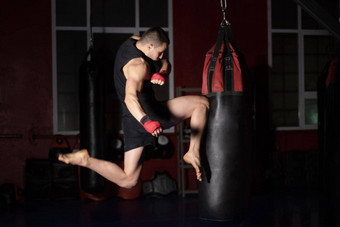 跆拳道战斗机执行跳空气踢膝盖穿孔袋高加索人男人。练习武术艺术培训城市健身房