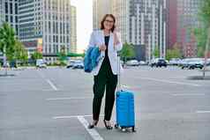 中间岁的业务女人手提箱会说话的移动电话户外停车