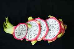 片龙水果火龙果粉红色的皮肤白色纸浆种子黑色的背景异国情调的水果健康的吃概念