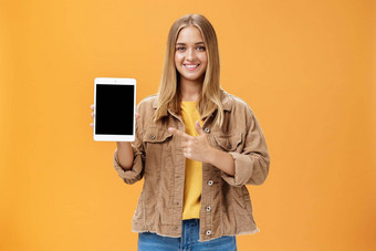 准备好了秋天semister数字平<strong>板</strong>电脑肖像迷人的女灯芯绒夹克显示小工具屏幕指出设备微笑很高兴友好的橙色墙