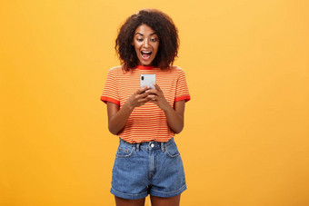女孩表达兴奋快乐接收太棒了邀请消息大喊大叫高兴的是幸福智能手机屏幕深刻的印象激动橙色背景