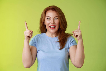 深刻的印象热情的快乐快乐的中年成熟的女人红色的头发微笑惊讶钦佩快乐指出提高了指数手指介绍令人印象深刻的惊人的提供绿色背景