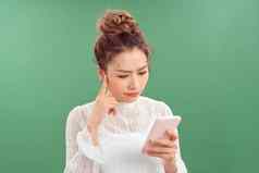 困惑年轻的亚洲女人智能手机站绿色背景