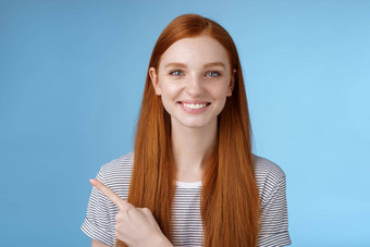 愉快的有魅力的有帮助的友善的女红色头发的人蓝色的眼睛指出左指数手指使决定选择产品商店微笑广泛的自信加沙相机信任