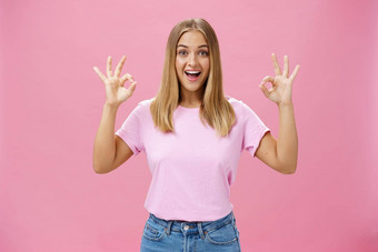 肖像热情的有吸引力的高加索人女孩时尚的t恤牛仔裤显示确认手势逗乐广泛的微笑站很高兴粉红色的背景反应优秀的新闻