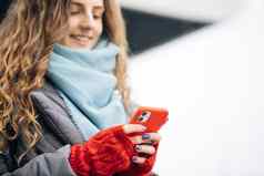肖像快乐的卷发年轻的女发短信智能手机站街冬天城市一年女攻丝手机在户外在线购物购买一年的礼物