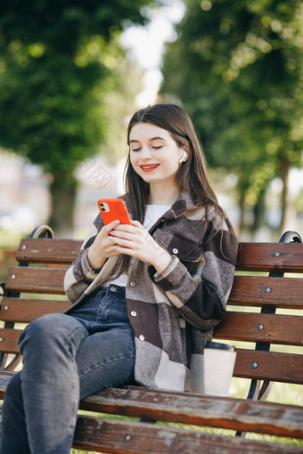 女孩穿耳机智能手机听音乐有吸引力的女人浏览移动电话公园城市城市背景