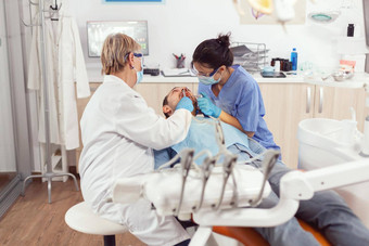 高级女人牙医分析牙齿检查生病的病人