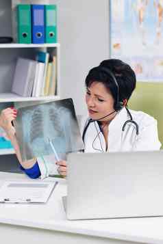 女医疗医生穿白色外套耳机视频调用遥远的病人移动PC医生会说话的客户端虚拟闲谈，聊天电脑应用程序远程医疗远程医疗保健服务概念
