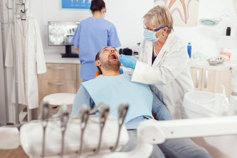 牙科高级女人医生使专业牙齿清洁生病的男人。