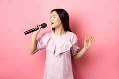 美丽的亚洲女孩执行首歌唱歌麦克风微笑浪漫的站衣服粉红色的背景