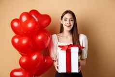 浪漫的女孩站心气球持有惊喜礼物情人节一天微笑相机快乐站米色背景