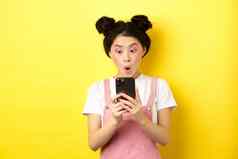 亚洲青少年女孩兴奋智能手机屏幕阅读新闻电话站黄色的背景