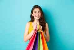 年轻的梦幻女人思考购买的事情持有购物袋微笑站蓝色的背景