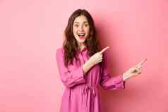 美时尚惊讶时尚的现代女人指出手指显示促销Copyspace站粉红色的背景