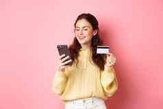技术在线购物年轻的漂亮的夫人支付在线信贷卡智能手机微笑站粉红色的背景