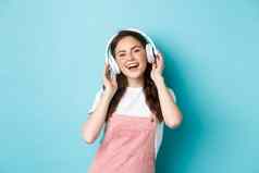 时尚的现代女孩听音乐无线耳机触碰耳机微笑唱歌站蓝色的背景