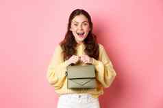 图像快乐年轻的女人购物持有钱包微笑兴奋准备好了站粉红色的背景