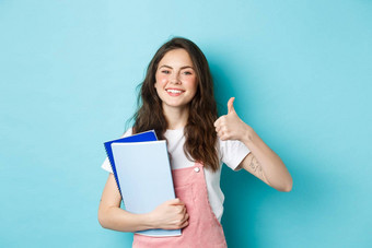 年轻的女人参加<strong>课程</strong>女孩学生研究持有笔记本电脑显示拇指批准推荐公司站蓝色的<strong>背景</strong>