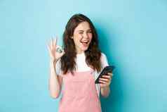 在线购物快乐的可爱的女孩眨眼微笑显示标志智能手机应用程序推荐互联网商店社会媒体页面蓝色的背景