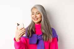 特写镜头时尚亚洲高级女人智能手机阅读消息微笑移动屏幕站白色背景