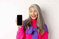 在线购物时尚的美丽的亚洲高级女人灰色头发显示空白智能手机屏幕很高兴站白色背景