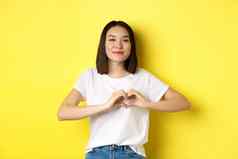 美丽的亚洲女人显示爱心手势微笑相机站黄色的背景概念情人节一天浪漫