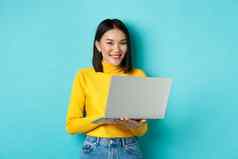 快乐亚洲女人黄色的套衫移动PC购物在线工作站蓝色的背景