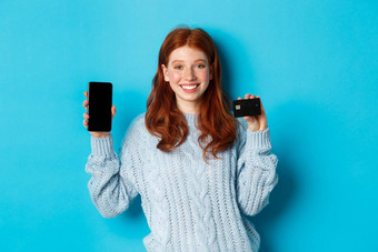 兴奋红色头发的人女孩显示移动电话屏幕信贷卡<strong>展示</strong>在线商店应用程序站<strong>蓝色</strong>的背景