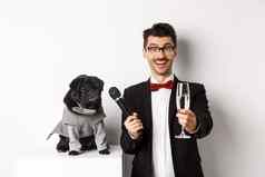 快乐的家伙提高玻璃香槟给麦克风狗服装庆祝享受聚会，派对站白色背景