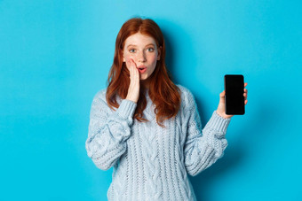 惊讶红色头发的人女孩相机显示智能手机屏幕展示在线提供站蓝色的背景
