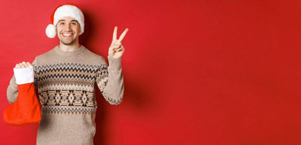 概念冬天假期一年庆祝活动图像快乐微笑男人。圣诞老人他毛衣显示和平标志圣诞节长袜袋礼物红色的背景