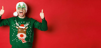 肖像超级快乐年轻的男人。聚会，派对眼镜圣诞老人他毛衣显示竖起大拇指批准推荐一年促销提供站红色的背景