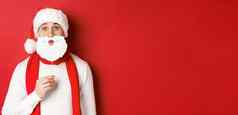 概念圣诞节冬天假期庆祝活动肖像有趣的男人。圣诞老人他持有胡子面具享受一年聚会，派对站红色的背景
