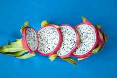 片龙水果火龙果粉红色的皮肤白色纸浆黑色的种子蓝色的背景异国情调的水果健康的吃概念
