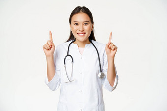 微笑亚洲女人医生穿医疗袍指出手指广告显示促销提供医疗保健信息白色背景