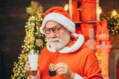 肖像有胡子的有趣的男人。圣诞老人服装圣诞老人有趣的圣诞老人老人吃饼干喝牛奶圣诞节夏娃圣诞节胡子风格
