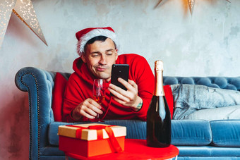 年轻的英俊的男人。圣诞老人老人他玻璃香槟采取自拍智能手机有趣的的家伙拍摄移动电话说谎沙发上概念圣诞节庆祝活动首页