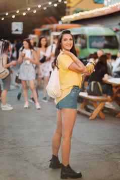 女孩黄色的衬衫短裤黑色的鞋子网柠檬柠檬汁走城市街女人鸡尾酒手