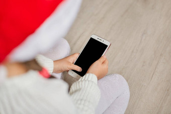 不知名的孩子持有电话空白屏幕摆姿势向后穿毛衣圣诞老人他坐着地板上移动电话视频调用玩游戏