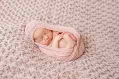 可爱的新生儿卷睡着了包装粉红色的尿布