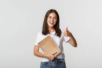 快乐的微笑女孩持有笔记本电脑显示竖起大拇指推荐课程学校