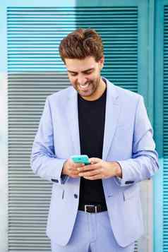 微笑男人。穿蓝色的西装发短信智能手机在户外