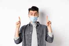 流感大流行生活方式医疗保健医学概念兴奋男人。广告医疗面具指出手指惊讶站白色背景