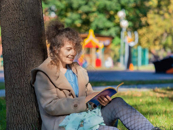 中年女人书公园坐着草阅读书概念休息小工具智能手机互联网