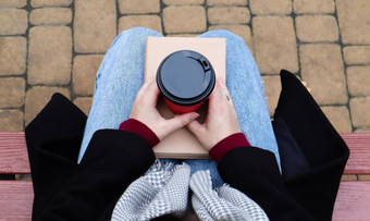 年轻的女人牛仔裤外套围巾公园板凳上女人阅读书喝咖啡热喝在户外特写镜头视图概念荣誉休闲