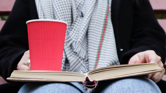 年轻的女人牛仔裤外套围巾公园板凳上女人阅读书喝咖啡热喝在户外特写镜头概念荣誉研究休闲娱乐
