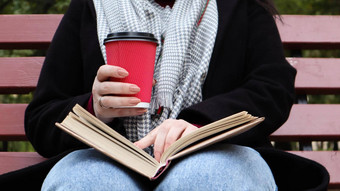 年轻的女人牛仔裤外套围巾公园板凳上女人阅读书喝咖啡热喝在户外特写镜头概念荣誉研究休闲娱乐