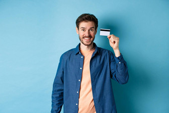 快乐高加索人的家伙微笑显示塑料信贷卡站休闲衣服蓝色的背景